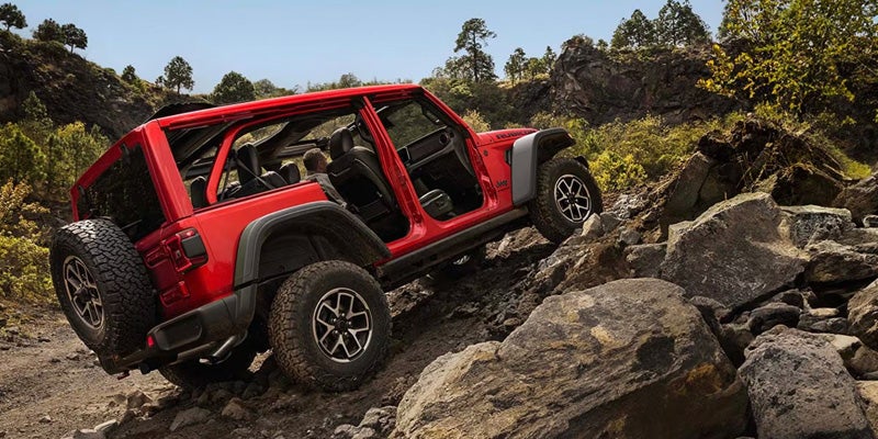 Red Jeep Wrangler with its doors off climbing a rocky trail.