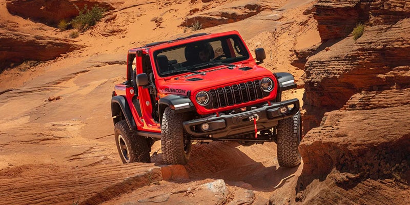 Red Jeep Wrangler Rubicon navigating rocky desert terrain during an off-road adventure.