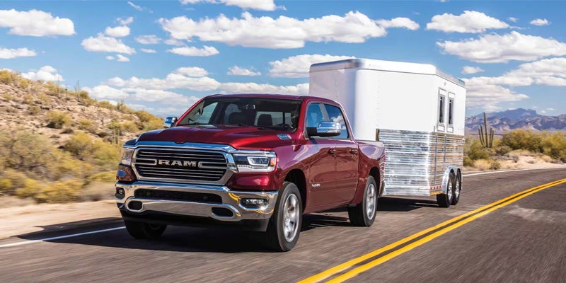Red Ram 1500 pickup truck towing a travel trailer on an open highway.