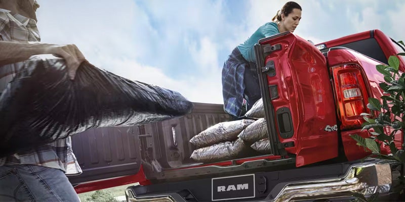 Person loading heavy bags into red pickup truck bed tailgate.