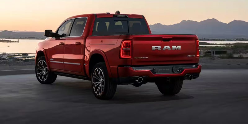Rear three-quarter view of a red Ram 1500 pickup truck parked near a waterfront at sunset.