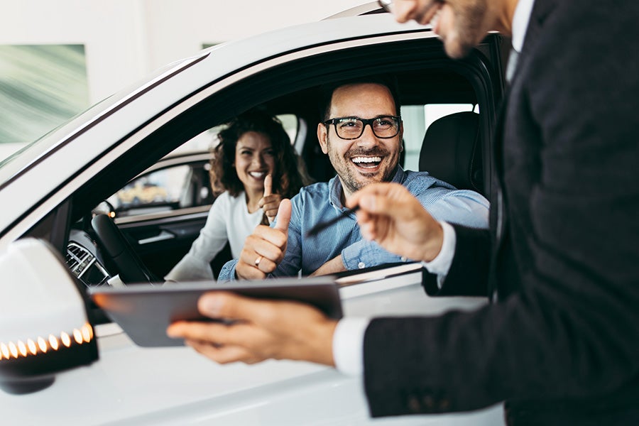 Car dealership consultant helping customers inspect a vehicle in a modern showroom