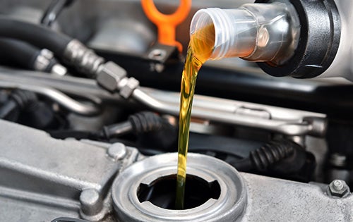 Fresh engine oil being poured into a vehicle engine during routine maintenance.