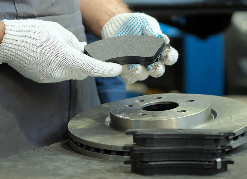 Technician inspecting and replacing brake pads and brake rotors during vehicle brake service.