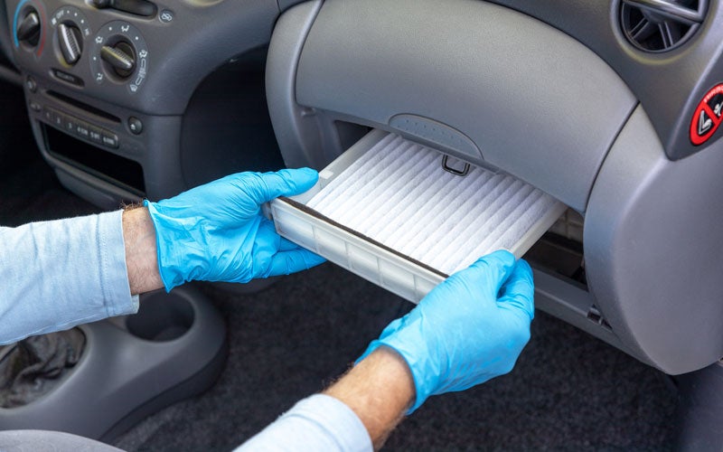 Technician replacing the cabin air filter inside a vehicle's glove compartment.