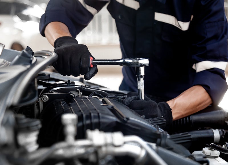 Close-up of a vehicle engine being serviced, with gloved hands using a socket wrench to tighten