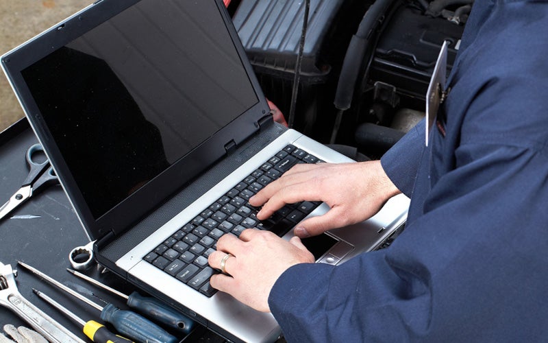 Technician using a laptop to perform vehicle diagnostics and maintenance checks.