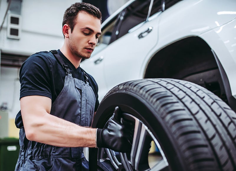 Automotive technician wearing work overalls and gloves installing or inspecting a vehicle tire in a garage