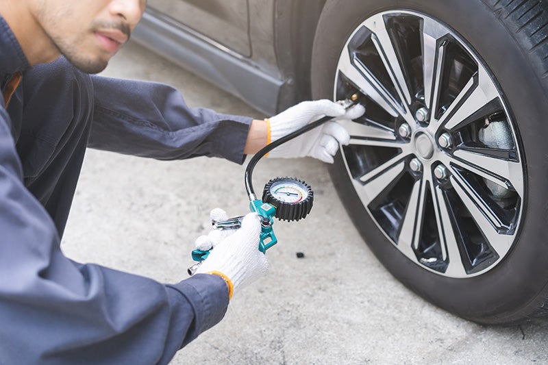 Technician checking and adjusting tire pressure using an air pressure gauge.